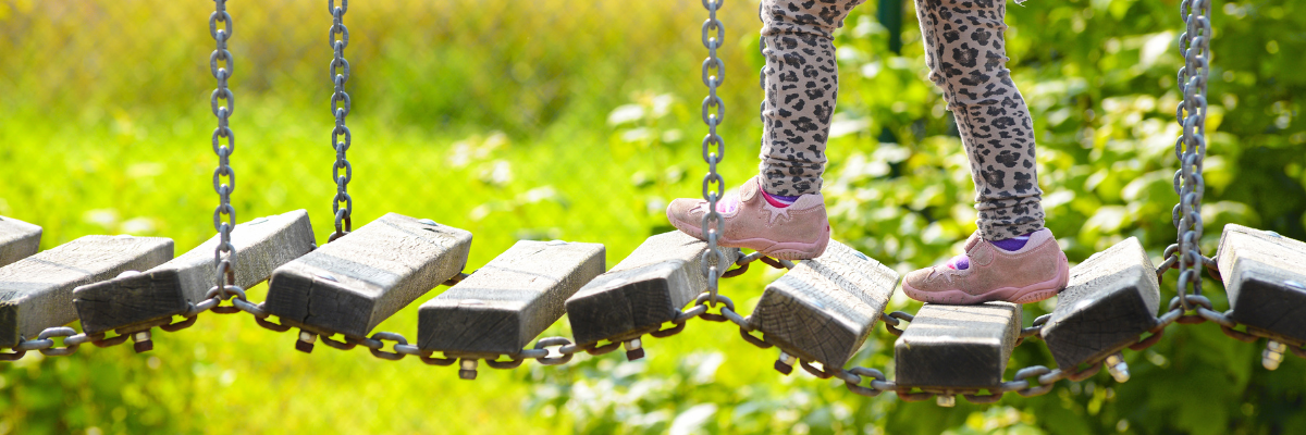 Child's legs walking over a playground bridge 